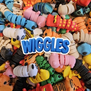 May include: A close-up of a collection of colourful, segmented toy caterpillars in shades of orange, pink, blue, and black. The word "Wiggles" is displayed in a blue, 3D font. The toys have a playful, whimsical design.