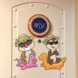 May include: A white door featuring a circular sign with the number 10552 and two cartoon chipmunks wearing straw hats and sunglasses. Each chipmunk sits on a colorful inflatable dinosaur pool float, one pink and one orange, on the door surface.