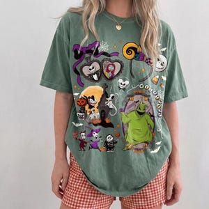 May include: Green t-shirt with a design featuring characters from "The Nightmare Before Christmas." The graphic includes Jack Skellington, Sally, Oogie Boogie, and other Halloween Town elements. The shirt has a relaxed fit and short sleeves.