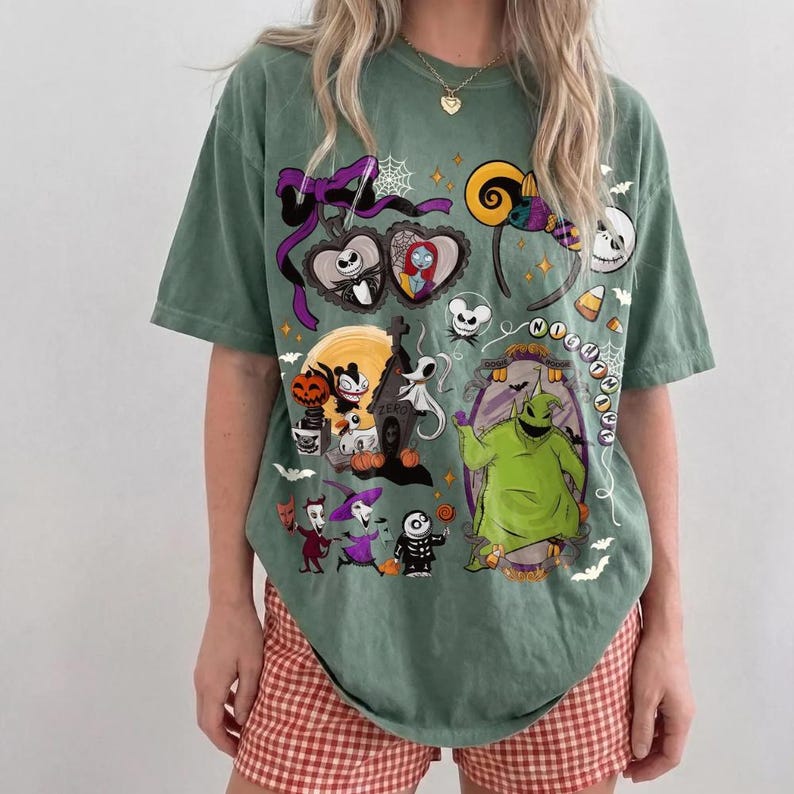 May include: Green t-shirt with a design featuring characters from "The Nightmare Before Christmas." The graphic includes Jack Skellington, Sally, Oogie Boogie, and other Halloween Town elements. The shirt has a relaxed fit and short sleeves.