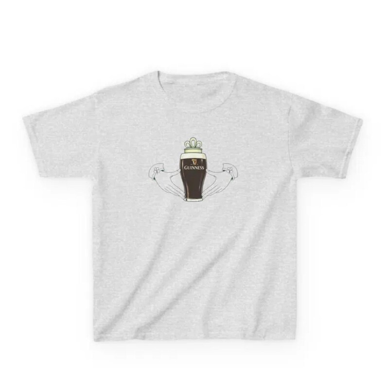 May include: A light grey t-shirt with a graphic of a pint of Guinness stout, a crown, and the word "Guinness". The pint is held by two hands, a traditional Irish symbol.
