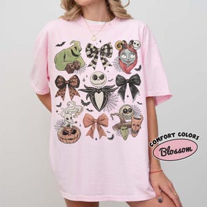 Puede incluir: Una camiseta de manga corta de color rosa claro con un estampado gr&aacute;fico de personajes y lazos de Pesadilla antes de Navidad. El dise&ntilde;o incluye a Oogie Boogie, Jack Skellington, Sally, Zero y varios lazos dispuestos en la parte frontal.