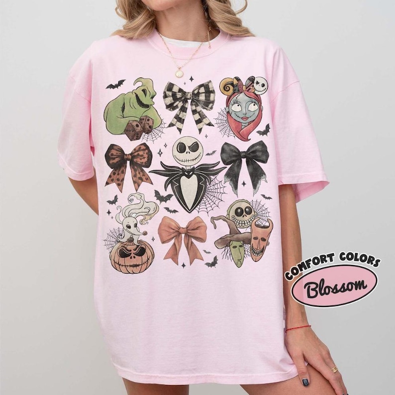 Puede incluir: Una camiseta de manga corta de color rosa claro con un estampado gr&aacute;fico de personajes y lazos de Pesadilla antes de Navidad. El dise&ntilde;o incluye a Oogie Boogie, Jack Skellington, Sally, Zero y varios lazos dispuestos en la parte frontal.