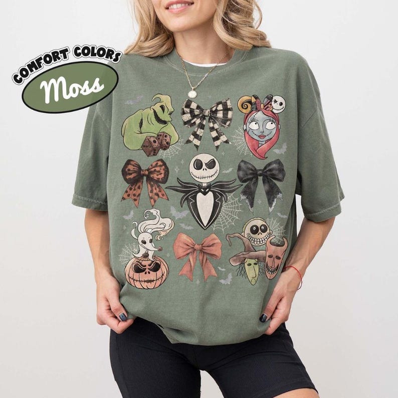 Puede incluir: Una camiseta verde musgo con un estampado gr&aacute;fico de personajes y lazos de Pesadilla antes de Navidad, incluyendo a Jack Skellington, Sally, Zero y Oogie Boogie, dispuestos con detalles de telara&ntilde;as y peque&ntilde;os murci&eacute;lagos en la tela.
