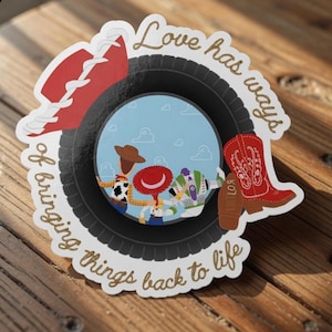 May include: A die-cut sticker featuring a black tire frame surrounding a scene of three cartoon characters. A red cowboy hat and a red cowboy boot are placed on the tire. The text "Love has ways of bringing things back to life" is written in gold.