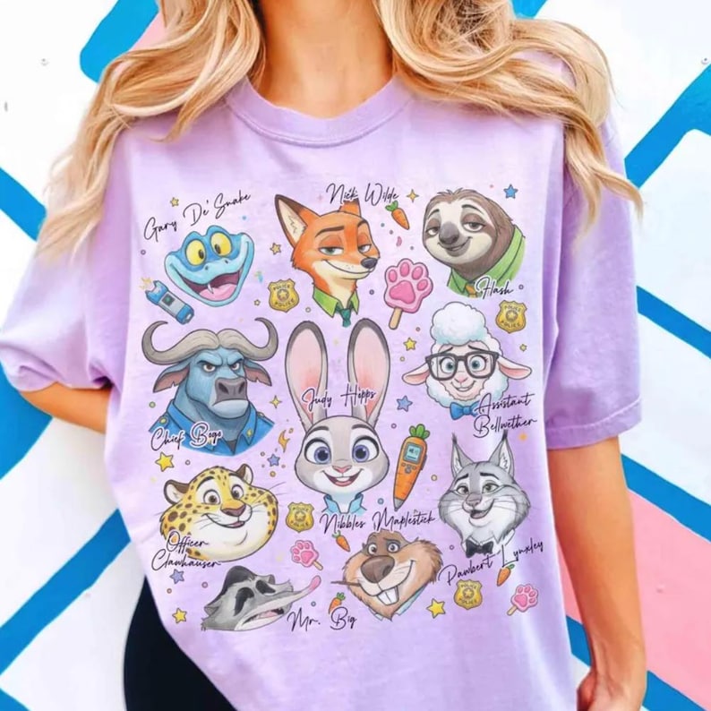 May include: A light purple t-shirt featuring cartoon characters from Zootopia. The design includes Judy Hopps, Nick Wilde, Flash, and other characters with their names. The shirt is a comfortable, casual style.