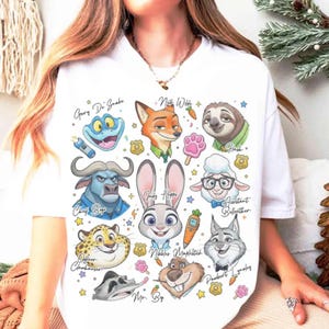 May include: White t-shirt featuring colorful cartoon illustrations of characters from the movie "Zootopia." The design includes characters like Judy Hopps, Nick Wilde, and Flash, with their names written above them. A fun and playful design.