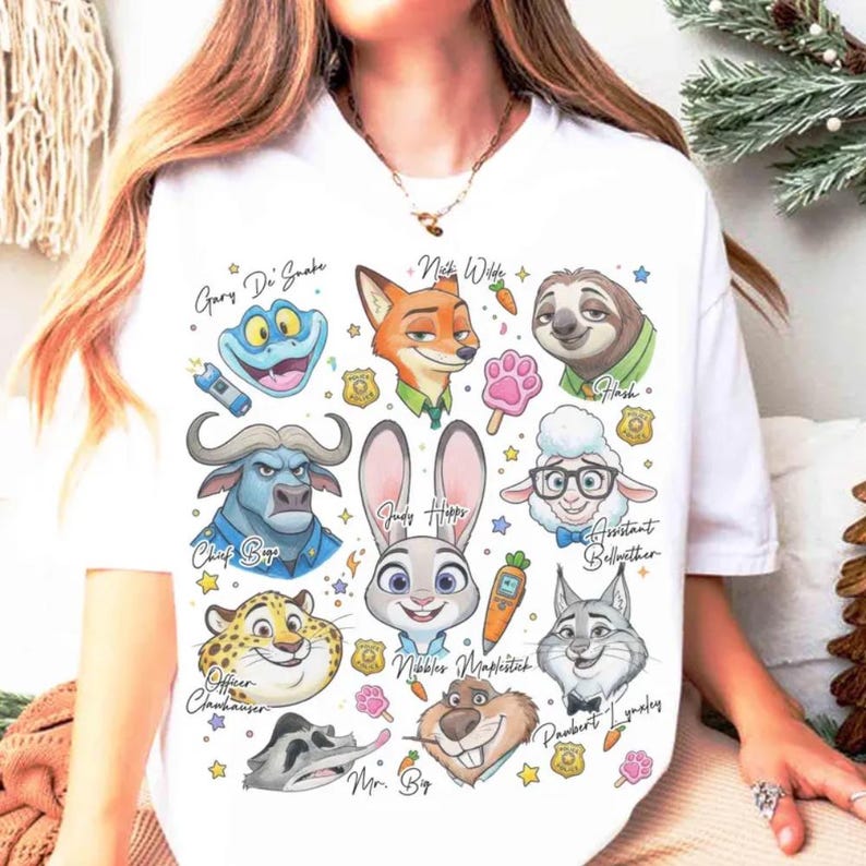 May include: White t-shirt featuring colorful cartoon illustrations of characters from the movie "Zootopia." The design includes characters like Judy Hopps, Nick Wilde, and Flash, with their names written above them. A fun and playful design.