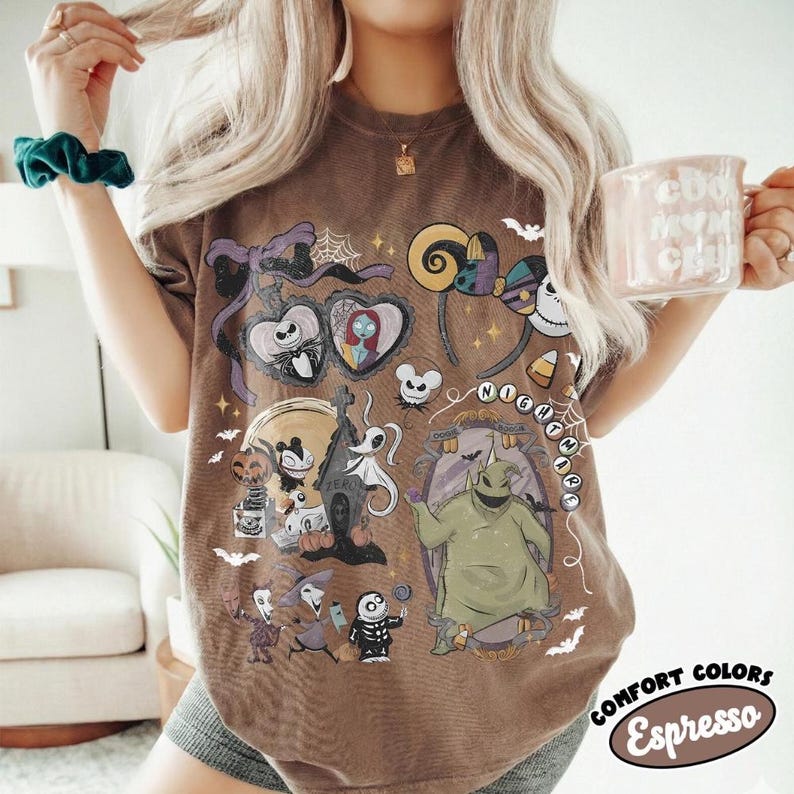 Op de afbeelding: Een bruin t-shirt met een grafische print van personages en motieven uit The Nightmare Before Christmas, waaronder Jack Skellington, Sally, Oogie Boogie en Zero. Het ontwerp bevat paarse strikken, spinnenwebben en de tekst Nightmare.