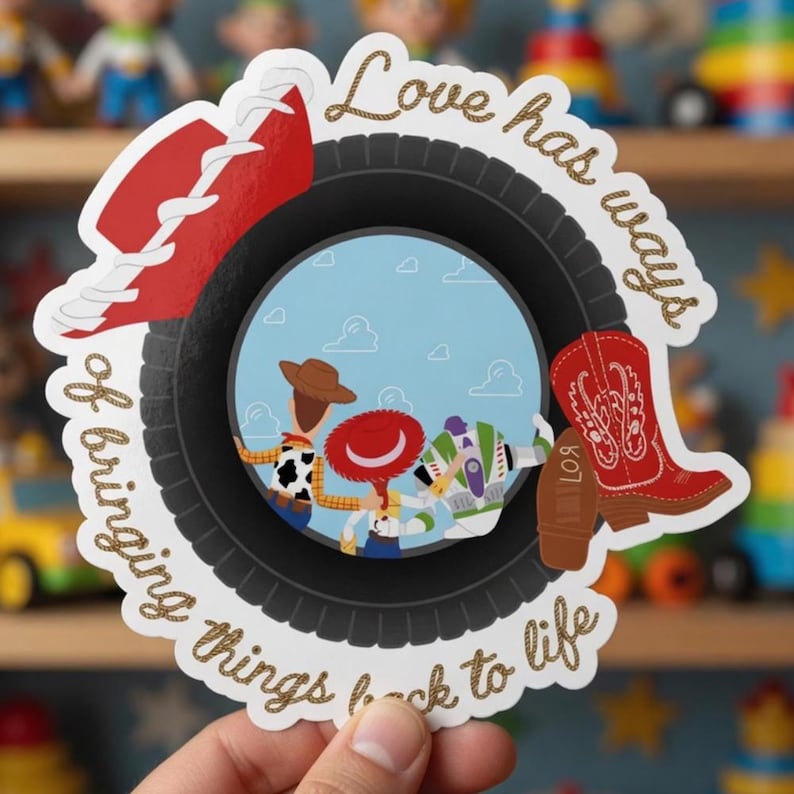May include: A die-cut sticker featuring a black tire frame surrounding a circular illustration of three cartoon characters. The text "Love has ways of bringing things back to life" is written in gold script. A red cowboy hat and a red boot are attached.