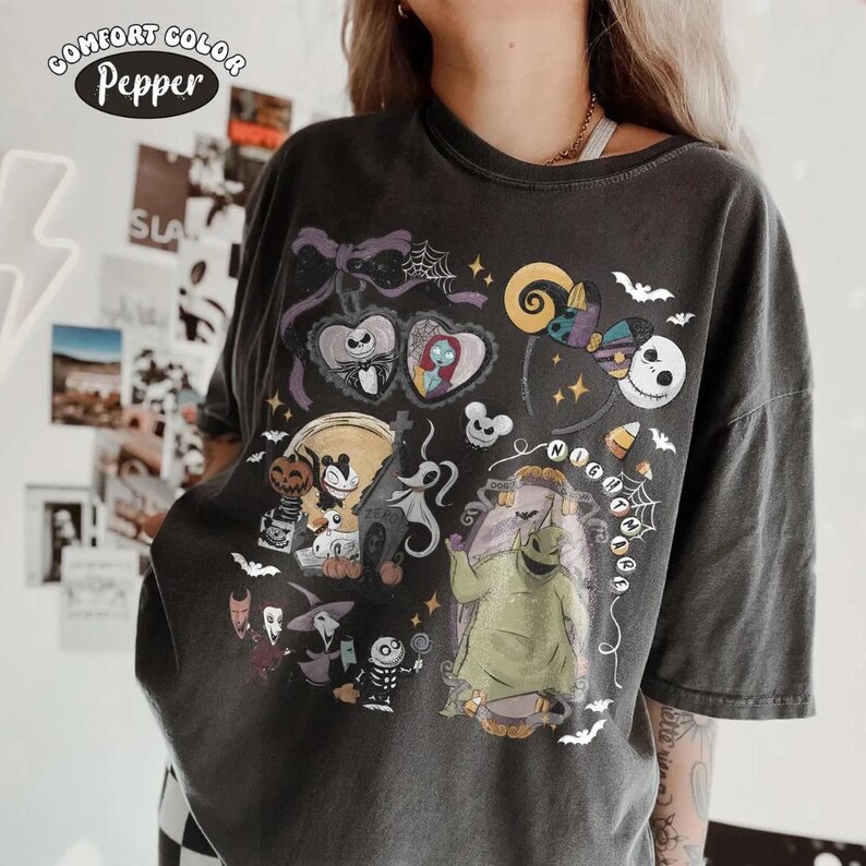 Op de afbeelding: Een antracietgrijs Comfort Colors Pepper T-shirt met een grafische print van personages uit The Nightmare Before Christmas, waaronder Jack Skellington, Sally, Oogie Boogie en Zero, omringd door vleermuizen, spinnenwebben en feestelijke iconen.