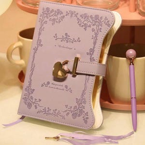 May include: A lavender-colored journal with a heart-shaped lock and key. The journal has a floral design and the text "Be the change that you wish to see in the world".