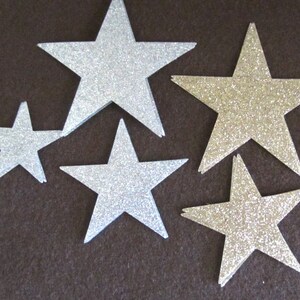 Op de afbeelding: Assortiment van zilveren glittersterren in verschillende maten. De sterren zijn uit papier geknipt en hebben een glinsterende afwerking.