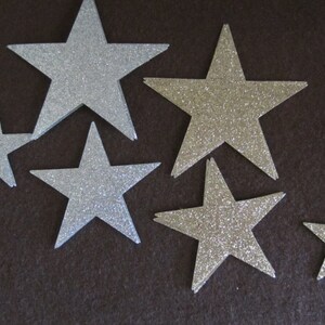 Op de afbeelding: Zes zilveren glittersterren in verschillende maten op een donkerbruine achtergrond.