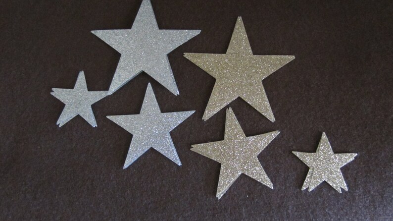 Op de afbeelding: Zes zilveren glittersterren in verschillende maten op een donkerbruine achtergrond.