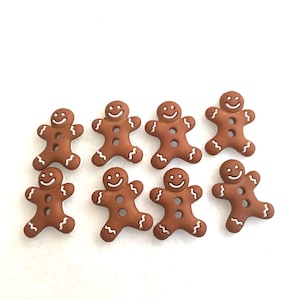 May include: Eight brown gingerbread man buttons with white icing details. The buttons have a smiling face and two white dots for eyes.