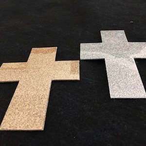 May include: Two glitter cross shapes, one gold and one silver, on a black background.