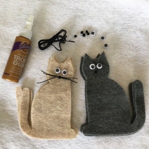 May include: Two felt cat shapes, one beige and one gray, with googly eyes and black yarn whiskers. A bottle of craft glue and a pile of extra googly eyes are also included.