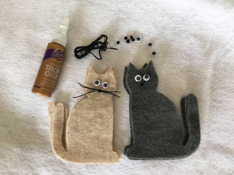 May include: Two felt cat shapes, one beige and one gray, with googly eyes and black yarn whiskers. A bottle of craft glue and a pile of extra googly eyes are also included.