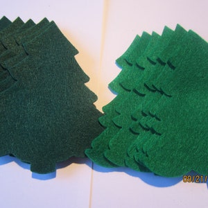 May include: A stack of green felt Christmas tree shapes. There are two stacks of trees, one on the left and one on the right.