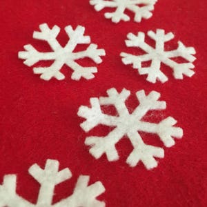 May include: Five white felt snowflakes on a red felt background. The snowflakes are different sizes and shapes.