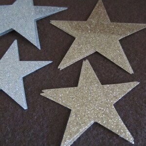 Op de afbeelding: Een verzameling zilveren en gouden glittersterren op een bruine achtergrond.