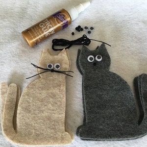 May include: Two felt cat shapes, one beige and one gray, with googly eyes, black yarn whiskers, and black thread for a tail.  A bottle of Aleene's Tacky Glue, a spool of black thread, and googly eyes are also included.