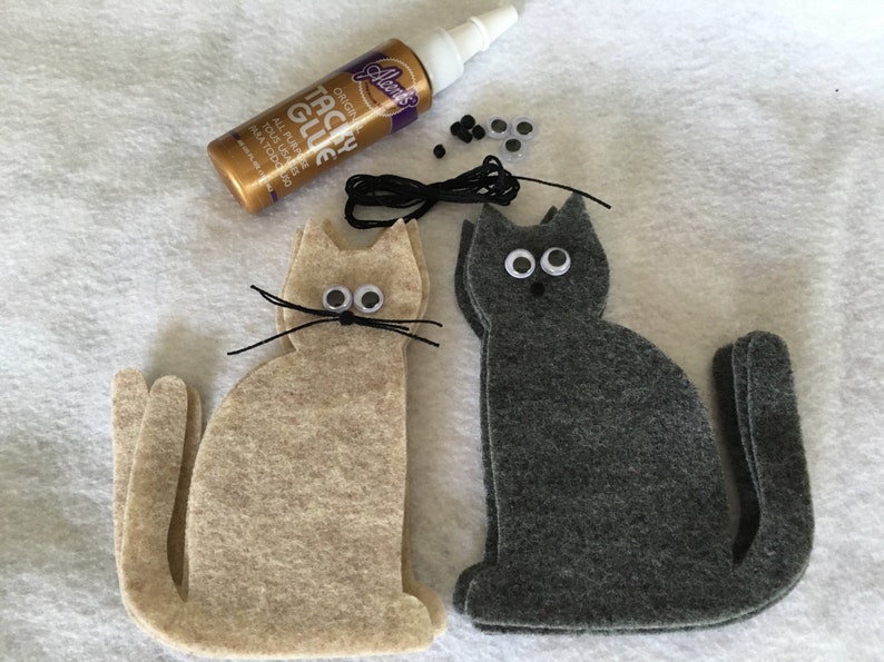 May include: Two felt cat shapes, one beige and one gray, with googly eyes, black yarn whiskers, and black thread for a tail.  A bottle of Aleene's Tacky Glue, a spool of black thread, and googly eyes are also included.