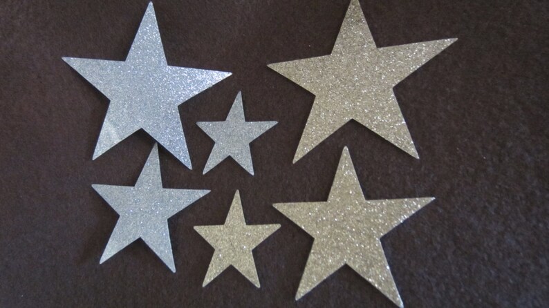 Op de afbeelding: Zes zilveren glittersterren in verschillende maten op een bruine achtergrond.
