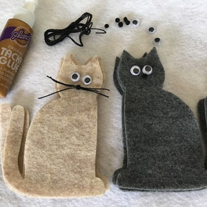 May include: Two felt cat shapes, one beige and one gray, with googly eyes and black yarn whiskers.  A bottle of Aleene's Tacky Glue, black yarn, and a pile of googly eyes are also included.
