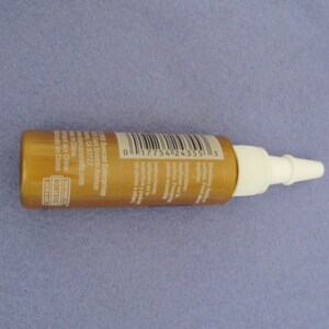 May include: A gold bottle with a white nozzle and a barcode label. The label includes the text "Duncan Enterprises", "East Shields Avenue", "CA 93727", "duncancrafts.com", "Made in China", and "NONTOXIC".