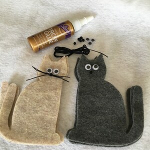 May include: Two felt cat shapes, one beige and one gray, with googly eyes, black yarn whiskers, and black thread for a tail. A bottle of tacky glue, black beads, and extra googly eyes are also included.