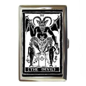 May include: A silver metal cigarette case with a black and white image of the Devil tarot card. The card depicts a horned figure with a pentagram on its chest, sitting on a throne with two chained figures at its feet. The text "XV THE DEVIL" is printed below the image.