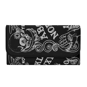 May include: Black wallet with a white Ouija board design. The design includes a skull, hand, and decorative swirls. The wallet has a bi-fold design with a snap closure.