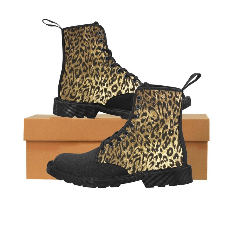 May include: Black canvas boots with a black and gold leopard print design. The boots have a lace-up closure and a thick, black rubber sole. The leopard print is by artist Shayne of the Dead. Shown with brown cardboard shoe box.
