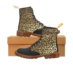 May include: Black canvas boots with a black and gold leopard print design. The boots have a lace-up closure and a thick, tan rubber sole. The leopard print is by artist Shayne of the Dead. Shown with brown cardboard shoe box.