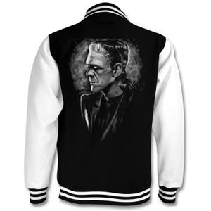 May include: Black and white varsity jacket with a graphic print of Frankenstein's monster on the back. The jacket has white sleeves and black body with white stripes on the collar and cuffs.