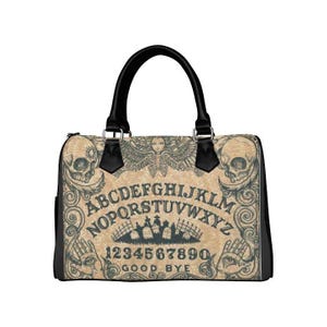 Può includere: Una borsa a mano nera con un design vintage di una tavola Ouija. La borsa presenta un teschio, ali d'angelo e le lettere e i numeri di una tavola Ouija. Il testo sulla borsa recita "ABCDEFGHIJKLMNOPQRSTUVWXYZ 1234567890 GOOD BYE".