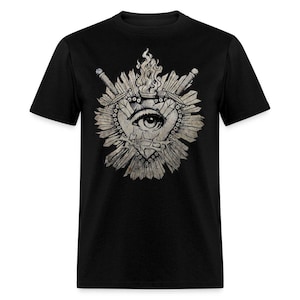 May include: Black t-shirt featuring a detailed graphic. The design includes an eye within a heart shape, crossed swords, and flames. The graphic is in shades of gray and white, creating a striking contrast against the black fabric.