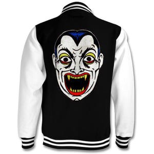 May include: A black and white varsity jacket with a white and black striped collar and cuffs. The back of the jacket features a colorful illustration of a vampire with fangs.