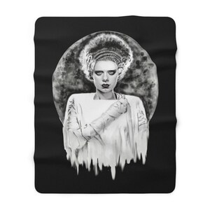 May include: Black and white throw blanket featuring a portrait of the Bride of Frankenstein. The image shows the Bride with her iconic hairstyle, makeup, and white dress. The background is a dark, smoky design.