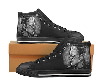 Pode incluir: Tênis de lona preto de cano alto com estampa gráfica do monstro Frankenstein. Os tênis têm cadarços brancos e uma faixa branca ao redor da sola.