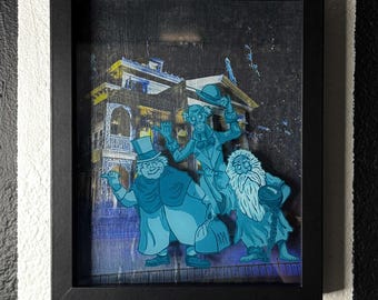 Könnte beinhalten: Gerahmtes Kunstwerk mit drei Cartoon-Geistern in Blautönen vor einem Spukhaus. Das Bild ist vor einem dunklen Hintergrund platziert und in einem schwarzen Schattenkasten gerahmt.
