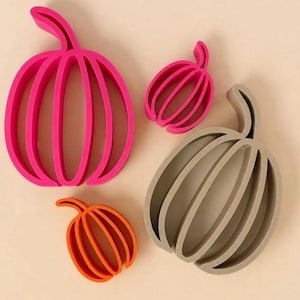 Könnte beinhalten: Ein Set aus vier kürbisförmigen Ausstechformen in verschiedenen Größen. Eine große Form ist leuchtend pink, eine mittlere Form ist beige und zwei kleinere Formen sind leuchtend pink und orange. Jede Form zeigt eine gerippte Kürbiskontur.