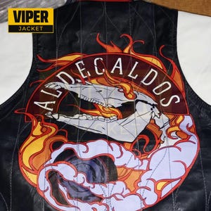 Puede incluir: Chaqueta de cuero negra con un gran parche bordado que presenta una calavera, llamas y el texto "ALDE CALDOS".
