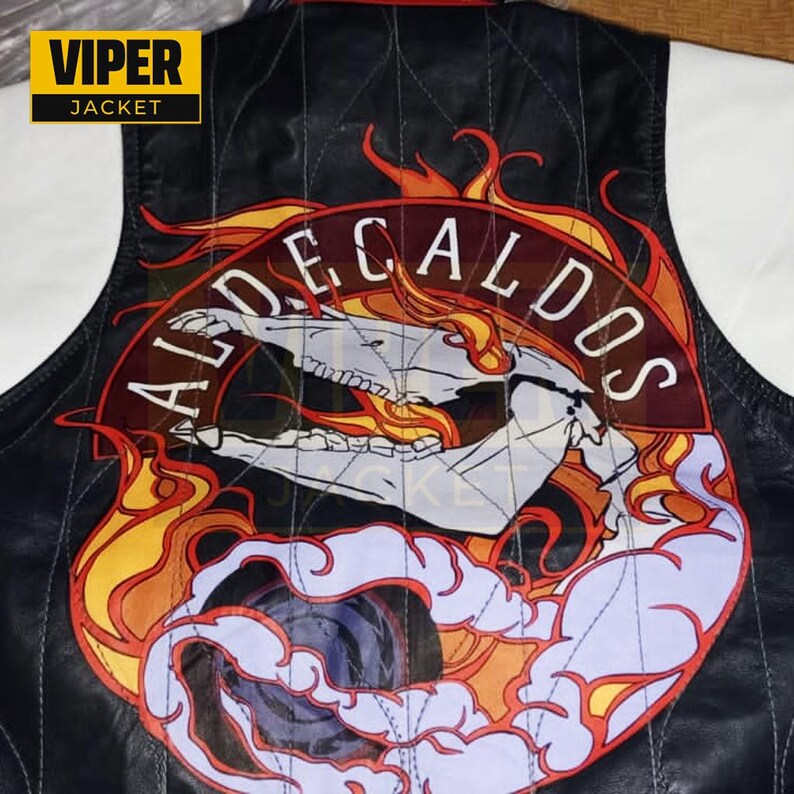 Puede incluir: Chaqueta de cuero negra con un gran parche bordado que presenta una calavera, llamas y el texto "ALDE CALDOS".