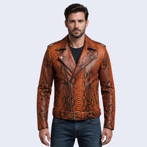 Puede incluir: Una chaqueta de motorista con un estampado de piel de serpiente en naranja y negro vibrante. La chaqueta incluye solapas con muescas, cierre de cremallera frontal asimétrico, bolsillos laterales con cremallera, charreteras y cinturón.