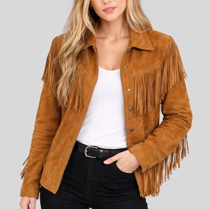 Puede incluir: Chaqueta de ante marrón con flecos en el pecho, hombros y mangas. La chaqueta tiene cierre de botones y cuello. La modelo lleva un top blanco y pantalones negros. La chaqueta es de estilo western clásico.