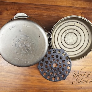 May include: An antique Griswold cast iron Dutch oven, with lid, base, and trivet, displayed on a wooden surface. The lid is marked "Tite-Top Dutch Oven" and "Griswold". The base is marked "Belf Basting". The trivet is black with multiple holes.