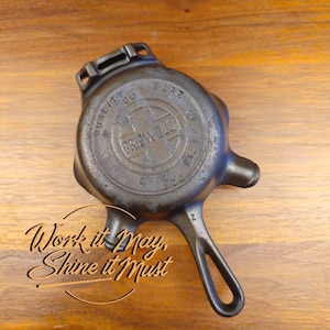 May include: Antique cast iron Griswold Ware skillet with a handle and a small spout. The skillet is dark gray with the text "Griswold" and "Quality Ware" embossed on the top. The text "Work it May, Shine it Must" is also visible.